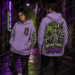 Puede incluir: Una sudadera con capucha de color morado claro que presenta un gr&aacute;fico de un personaje con traje a rayas, una serpiente y el texto "NEVER TRUST THE LIVING" en la espalda, con un gr&aacute;fico m&aacute;s peque&ntilde;o del "Handbook for the Recently Deceased" en el pecho.