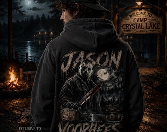 May include: A dark gray hooded sweatshirt featuring a graphic print on the back. The design depicts a hockey-masked figure holding a knife, with the text "JASON VOORHEES" in a distressed font. The scene includes a forest, a full moon, and a lake.