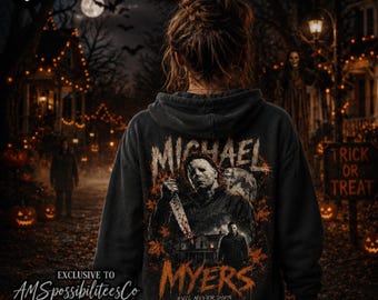 May include: A black hooded sweatshirt featuring a graphic print of Michael Myers holding a knife, with the text "MICHAEL MYERS" and "EVIL NEVER DIES" in orange, surrounded by autumn leaves and a house silhouette on the back of the garment.