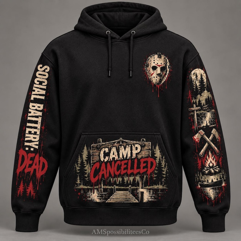 May include: A black hooded sweatshirt featuring a hockey mask graphic on the chest, the text "CAMP CANCELLED" on a wooden sign, "SOCIAL BATTERY: DEAD" on the left sleeve, and a forest, axes, and campfire scene on the right sleeve.