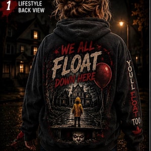 Puede incluir: Una sudadera con capucha gris oscuro que presenta un gráfico en la espalda de un niño con impermeable amarillo frente a una casa, con el texto WE ALL FLOAT DOWN HERE y un globo rojo. La manga muestra el texto YOU'LL FLOAT TOO con un barco de papel rojo.