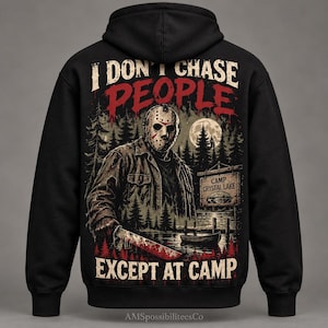 May include: A black hooded sweatshirt featuring a graphic on the back of a hockey-masked figure holding a machete. The text reads I DON'T CHASE PEOPLE EXCEPT AT CAMP. The scene includes a forest, a full moon, a boat, and a sign for CAMP CRYSTAL LAKE.