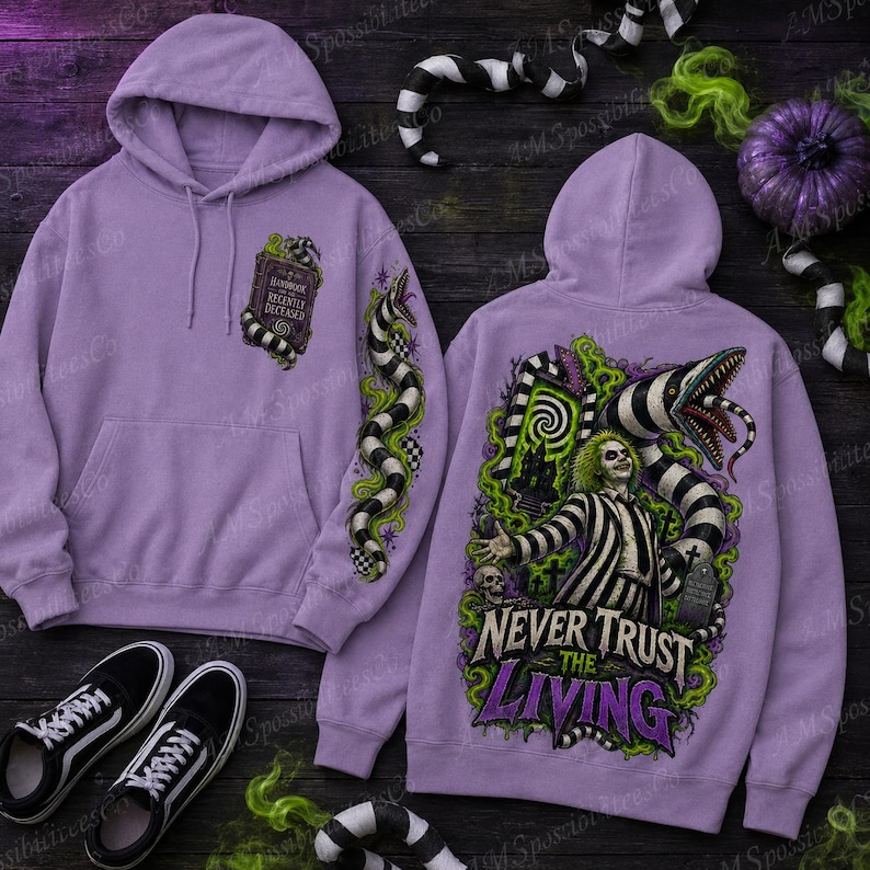 Puede incluir: Una sudadera con capucha de color morado claro que presenta un gr&aacute;fico frontal de un libro titulado Handbook for the Recently Deceased y un gr&aacute;fico trasero de un personaje con traje a rayas con el texto Never Trust the Living rodeado por una serpiente.