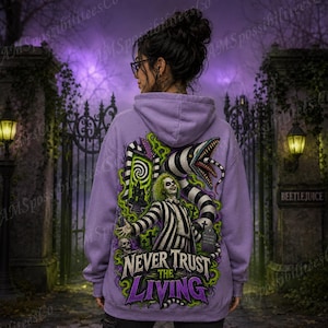 Puede incluir: Una sudadera con capucha de color morado claro que presenta un estampado gr&aacute;fico en la espalda de un personaje con traje de rayas blancas y negras, una serpiente grande a rayas y humo verde. El texto dice NEVER TRUST THE LIVING.