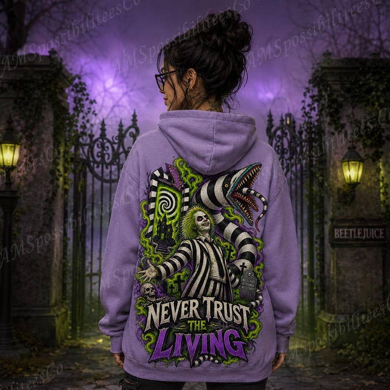 Puede incluir: Una sudadera con capucha de color morado claro que presenta un estampado gr&aacute;fico en la espalda de un personaje con traje de rayas blancas y negras, una serpiente grande a rayas y humo verde. El texto dice NEVER TRUST THE LIVING.