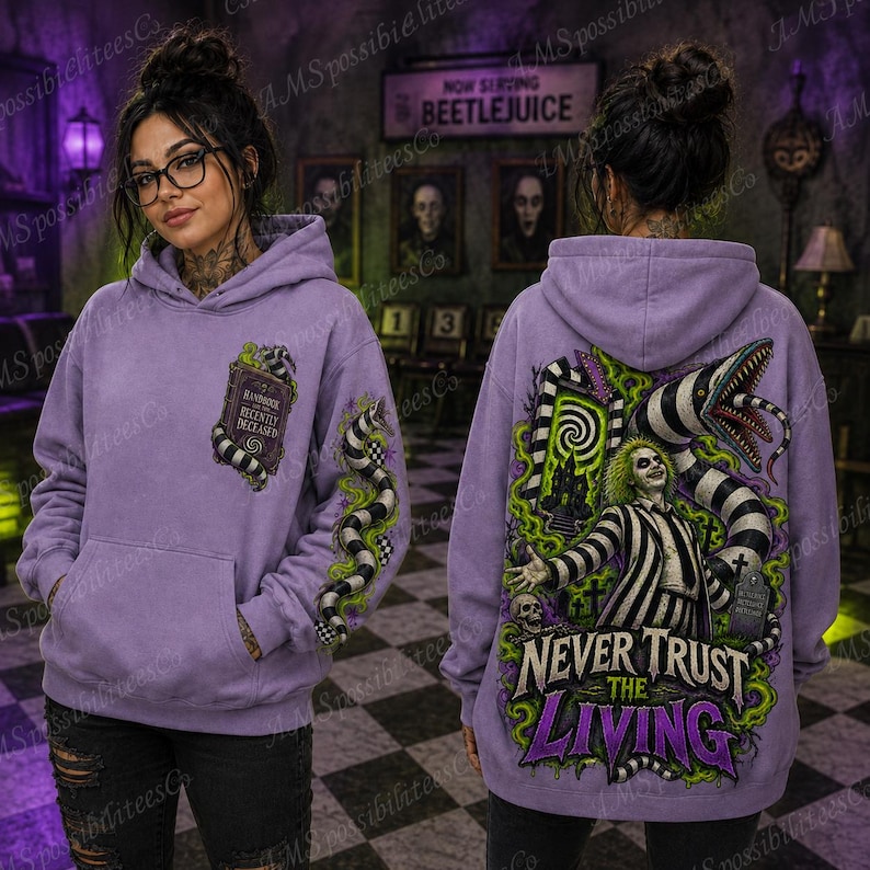 Puede incluir: Una sudadera con capucha color lavanda que presenta un gr&aacute;fico del Handbook for the Recently Deceased en el frente. La parte posterior muestra una ilustraci&oacute;n de Beetlejuice con un gusano de arena, un cementerio y el texto Never Trust the Living.