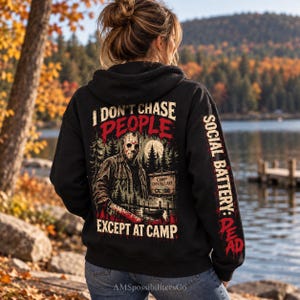 May include: A black hooded sweatshirt featuring a graphic on the back of a hockey-masked figure holding a bloody machete near a sign that reads Camp Crystal Lake. The text reads I DON'T CHASE PEOPLE EXCEPT AT CAMP and SOCIAL BATTERY: DEAD.