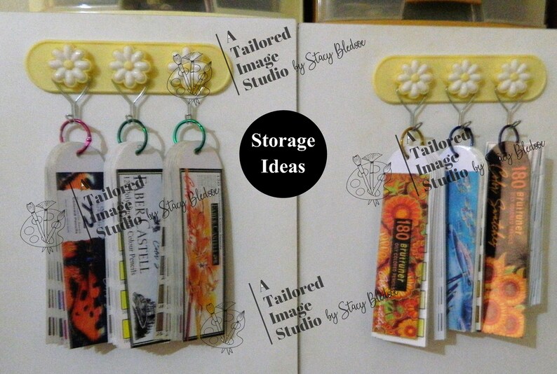 May include: A white wall with two rows of colorful, hanging, labeled, storage containers. The containers are labeled "Tailored Image Studio" and "180 Brutruner". The containers are hanging from a yellow bar with three white daisy-shaped hooks.