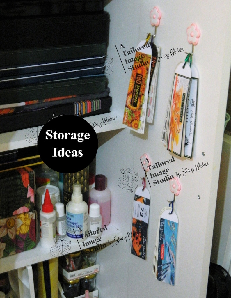 May include: A white shelf with various items, including bottles of liquid, a stack of black notebooks, and several colorful bookmarks hanging from hooks. The bookmarks are labeled "A Tailored Image Studio by Stacy Bledsoe" and feature different designs, including a butterfly, a flower, and a cityscape. The text "Storage Ideas" is written in black on a white background.