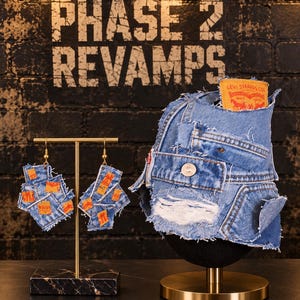 May include: A bucket hat and a pair of matching earrings crafted from repurposed blue denim fabric. The hat features a prominent orange Levi Strauss & Co. brand patch, frayed edges, and a metal button. The earrings display small orange fabric tags.
