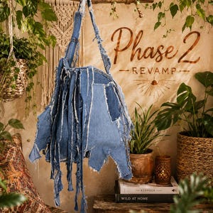 May include: A denim tote bag with a patchwork design and frayed edges hangs from a wooden branch. The bag is made of various shades of blue denim. The background features the text "Phase 2 - REVAMP".