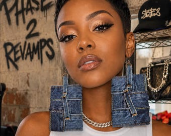 May include: Large square-shaped earrings constructed from dark blue denim fabric with visible stitching and belt loop details. The earrings feature a flat, geometric design with frayed edges and are suspended from thin metal hooks.