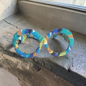 Puede incluir: Un par de gafas decorativas con una envoltura de tela colorida. La tela presenta un patrón de azul, amarillo y marrón. Las gafas están sobre una superficie de madera desgastada cerca de una ventana.