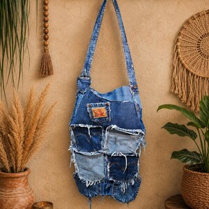 May include: A shoulder bag constructed from repurposed blue denim fabric, featuring a patchwork design with multiple visible pockets, frayed edges, and a rectangular leather-style brand patch on the front pocket. It has a single long denim strap.