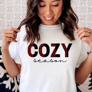Op de afbeelding: Wit T-shirt met de tekst "COZY season" in zwarte letters met een rood-zwart buffalo plaid patroon.