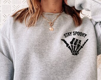 Może przedstawiać: Szara bluza z czarnym nadrukiem szkieletu dłoni i napisem "Stay Spooky" z przodu.