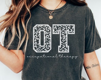 May include: A dark gray t-shirt with a white graphic of the letters "OT" in a leopard print design. The text "occupational therapy" is written below the letters.