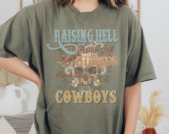 Puede incluir: Camiseta verde con un gráfico de calavera y el texto "Raising Hell with the Hippies and the Cowboys".