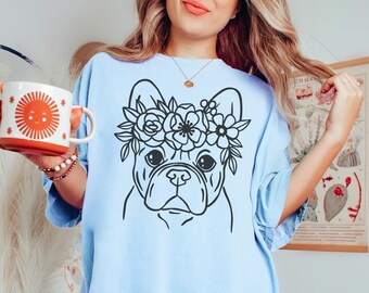 Puede incluir: Una camiseta azul claro con un dibujo en línea negra de un bulldog francés con una corona de flores.