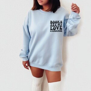 May include: A light blue sweatshirt with the text "BOOKS ARE MY LOVE LANGUAGE" printed in black on the front.