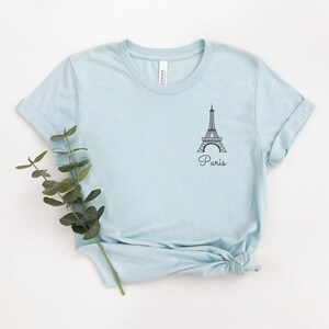 May include: A light blue t-shirt with a black outline of the Eiffel Tower and the word "Paris" printed on the front.
