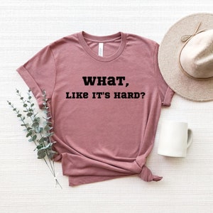 May include: A mauve t-shirt with the text "WHAT, LIKE IT'S HARD?" printed in black.