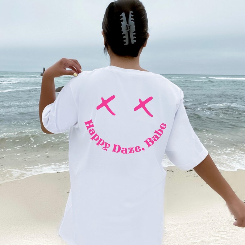 May include: White t-shirt with a pink smiley face graphic and the text "Happy Daze, Babe" on the back.