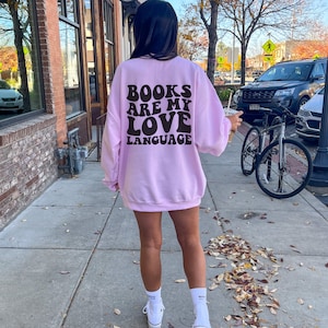 May include: A pink sweatshirt with the text "BOOKS ARE MY LOVE LANGUAGE" in black retro-style lettering on the back.