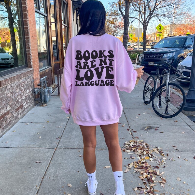 May include: A pink sweatshirt with the text "BOOKS ARE MY LOVE LANGUAGE" in black retro-style lettering on the back.