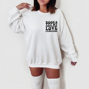 May include: White sweatshirt with black text that reads "BOOKS ARE MY LOVE LANGUAGE" in a retro font.