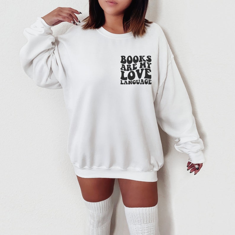 May include: White sweatshirt with black text that reads "BOOKS ARE MY LOVE LANGUAGE" in a retro font.