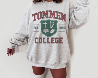 May include: A light gray sweatshirt with the text "TOMMEN COLLEGE" in red and green. The design includes a shield with a cross, harp, book, and football. The sweatshirt has a crew neck and long sleeves.