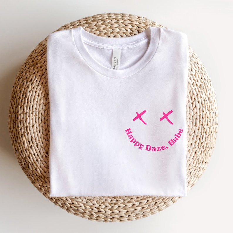 May include: White t-shirt with a pink smiley face graphic and the text "Happy Daze, Babe".