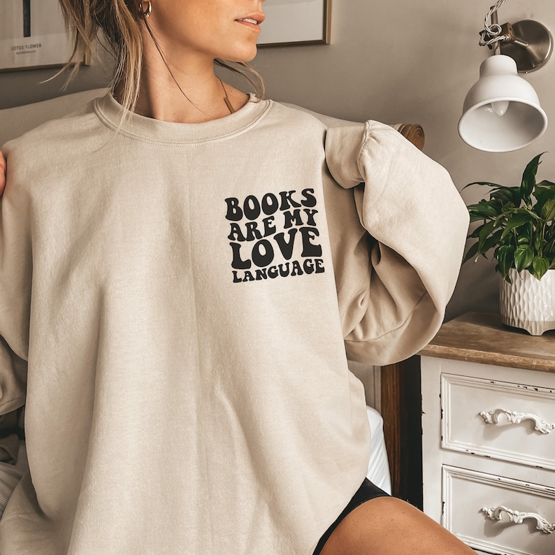 May include: A beige sweatshirt with a black graphic that reads "BOOKS ARE MY LOVE LANGUAGE" in a retro font.