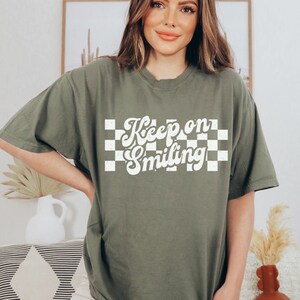 May include: A green t-shirt with a white checkered background and the text "Keep on Smiling" in a retro font.