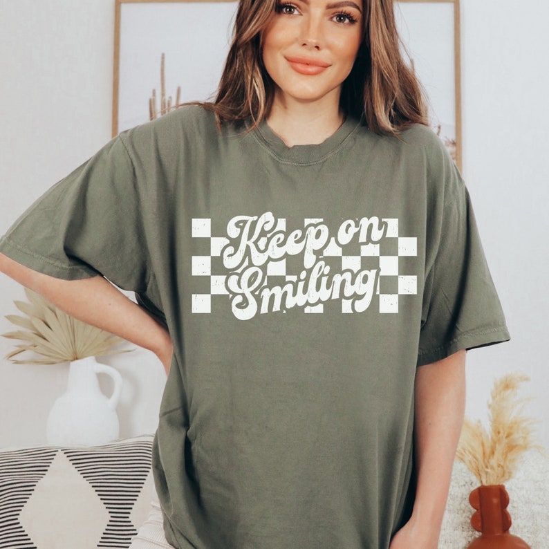 May include: A green t-shirt with a white checkered background and the text "Keep on Smiling" in a retro font.