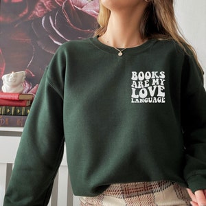 May include: A dark green sweatshirt with a white graphic that says "Books are my love language" in a retro font.