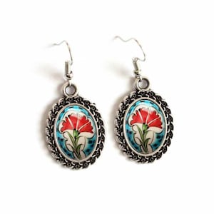 May include: A pair of silver earrings with a blue and white enamel design featuring a red flower. The earrings have a delicate chain design around the edge.