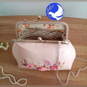 May include: A pink fabric purse with a floral embroidery design and a silver chain strap. The purse is open and the inside is lined with a floral print fabric and lace.