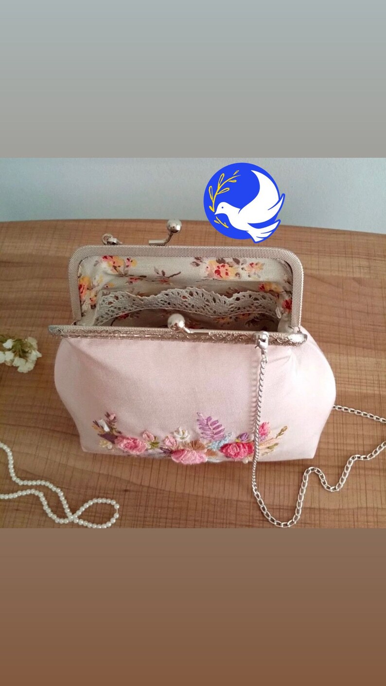 May include: A pink fabric purse with a floral embroidery design and a silver chain strap. The purse is open and the inside is lined with a floral print fabric and lace.