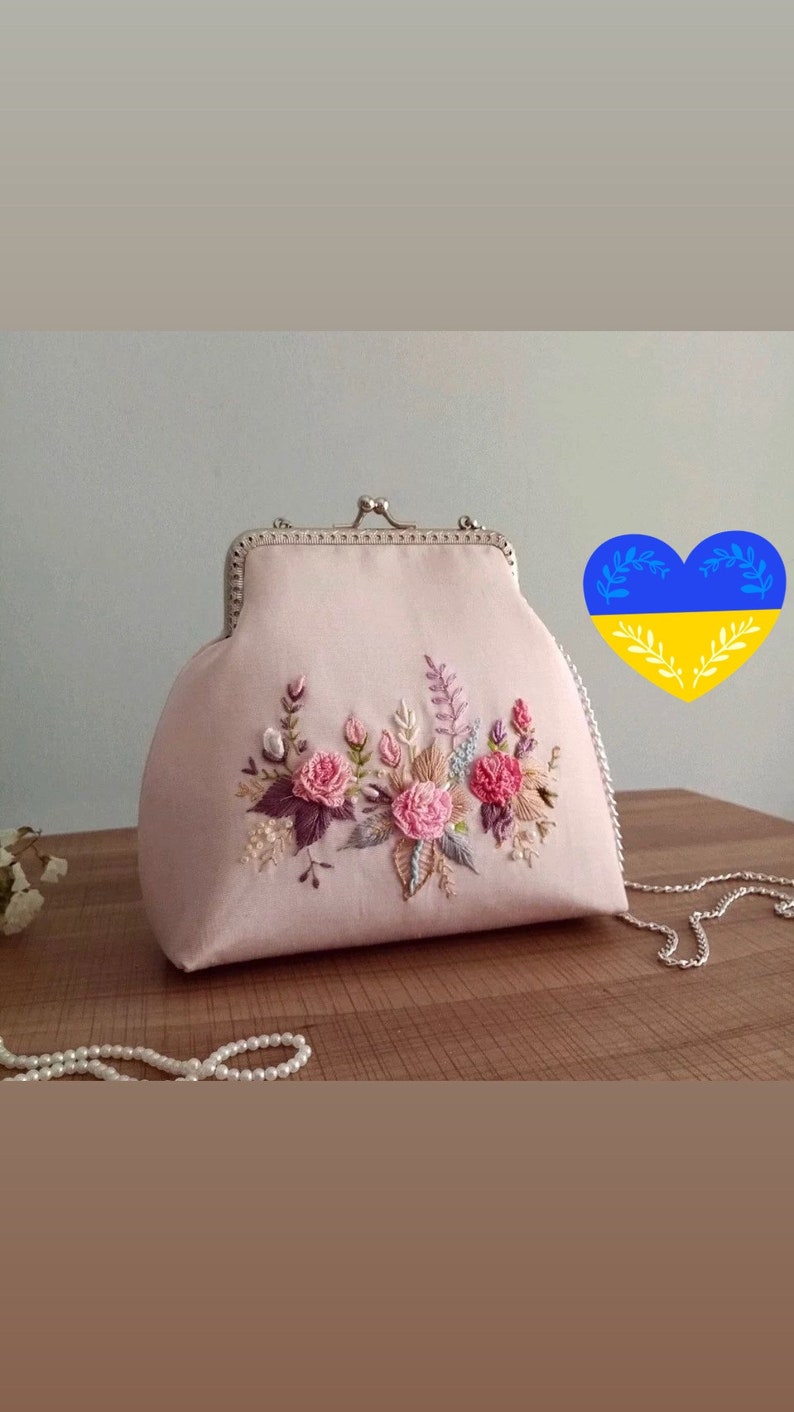 May include: A pink satin clutch bag with a silver clasp and chain strap. The bag is decorated with embroidered flowers in shades of pink, purple, and green.