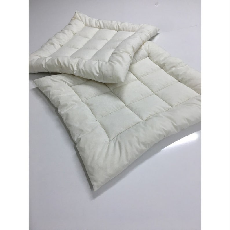 May include: Two white quilted square cushions, one on top of the other. The cushions are made of a soft, plush fabric and have a subtle sheen.