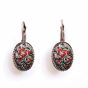 May include: A pair of copper-toned earrings with oval-shaped black and white glass cabochons featuring a red floral design.
