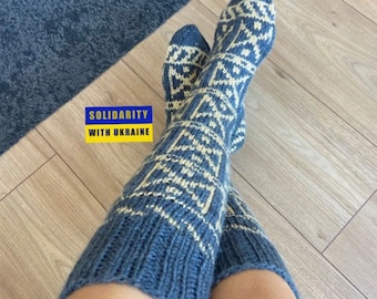 May include: A pair of blue and white knitted knee-high socks with a geometric pattern. The socks are worn by a person and the image includes the text "Solidarity with Ukraine".