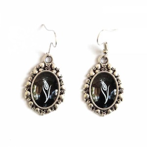 May include: A pair of silver earrings featuring a black background and a white tulip design. The earrings have a detailed, ornate design.