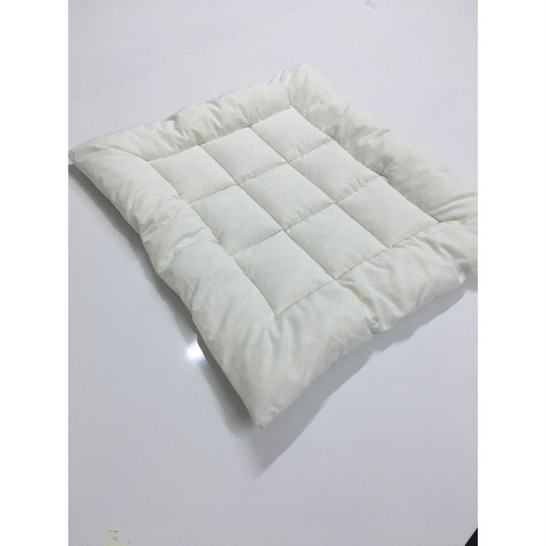 May include: A white quilted square cushion with a soft, plush texture. The cushion is made of a lightweight fabric and has a simple, modern design.
