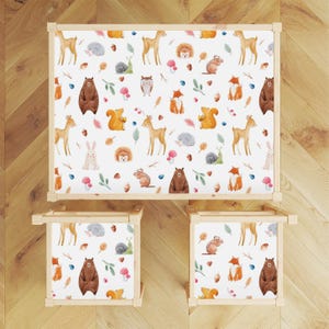 May include: A white wooden table and two chairs with a woodland animal print design. The print features deer, squirrels, foxes, bears, owls, and hedgehogs in shades of brown, orange, and gray.