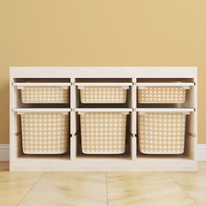 May include: A white wooden storage unit with six cubbies, each holding a beige and white gingham patterned bin. The bins have white rims and are arranged in two rows of three. The background is a solid light yellow.