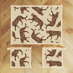 May include: A set of wooden furniture comprising a table and two chairs. The table and chairs are covered in a cream-coloured fabric with a repeating pattern of brown cheetahs.