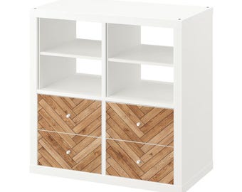 May include: White cube storage unit with four open compartments and four drawers. The drawer fronts feature a herringbone wood grain pattern. Each drawer has a small, round, silver-colored knob. The unit is designed for home organization.